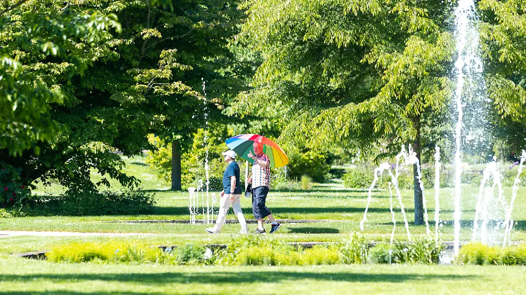 Die-ersten-Besucher-geniessen-bei-sommerlichen-29-Grad-den-Rosengarten-im-rheinland-pfaelzischen-Zweibruecken-Ein-Mann-schuetzt-sich-dabei-mit-einem-Sonnenschirm-vor-der-Sonne