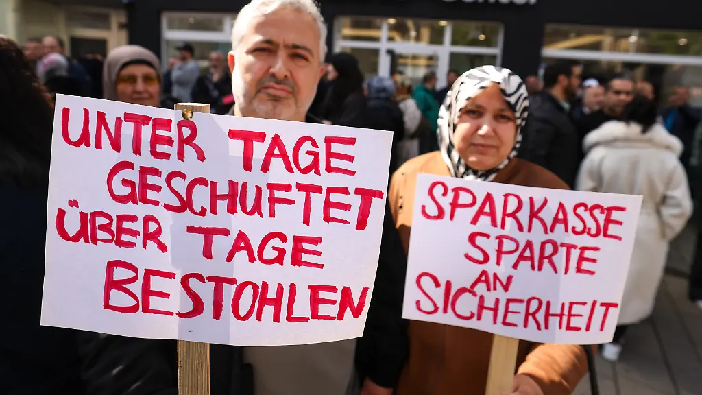 Teilnehmer-einer-Demonstration-halten-Schilder-in-den-Haenden-sie-demonstrieren-gegen-das-Verhalten-der-Sparkasse