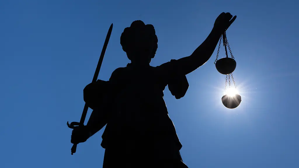 Die-Silhouette-der-Justitia-Statue-auf-dem-Roemerberg-in-Frankfurt-am-Main-zeichnet-sich-gegen-Sonne-ab-Dabei-hat-es-den-Anschein-als-laege-die-Sonne-in-Ihrer-Gerechtigkeitswaage
