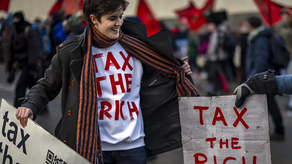 Die-deutsch-oesterreichische-Millionaerserbin-und-Sozialaktivistin-Marlene-Engelhorn-haelt-ein-Plakat-mit-der-Aufschrift-Tax-the-rich-Besteuert-die-Reichen-auf-einer-Demonstration-vor-dem-jaehrlichen-Treffen-des-Weltwirtschaftsforums-WEF-in-Davos-Schweiz-Millionaere-und-Milliardaere-haben-auf-dem-Weltwirtschaftsforum-in-Davos-hoehere-Steuern-fuer-Superreiche-wie-sie-selbst-gefordert-Rund-370-Unterzeichner-warnten-in-einem-offenen-Brief-an-die-Staats-und-Regierungschefs-dass-extremer-Reichtum-eine-Gefahr-fuer-die-Demokratie-sei-weil-er-oft-mit-politischem-Einfluss-einhergehe