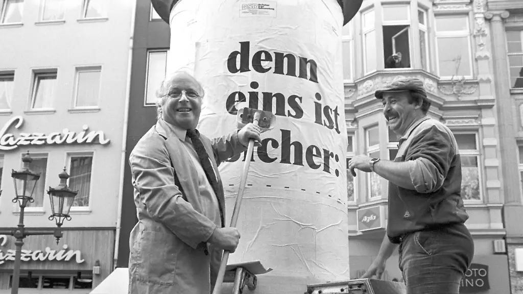 Eigenhaendig-geift-Bundesarbeitsminister-Norbert-Bluem-am-21-4-1986-auf-dem-Bonner-Marktplatz-zum-Leimpinsel-um-das-erste-Plakat-einer-Informations-Aktion-zur-Sicherheit-der-Renten-auf-eine-Litfasssaeule-zu-kleben-Der-Text-des-Plakates-lautet-denn-eins-ist-sicher-Die-Rente