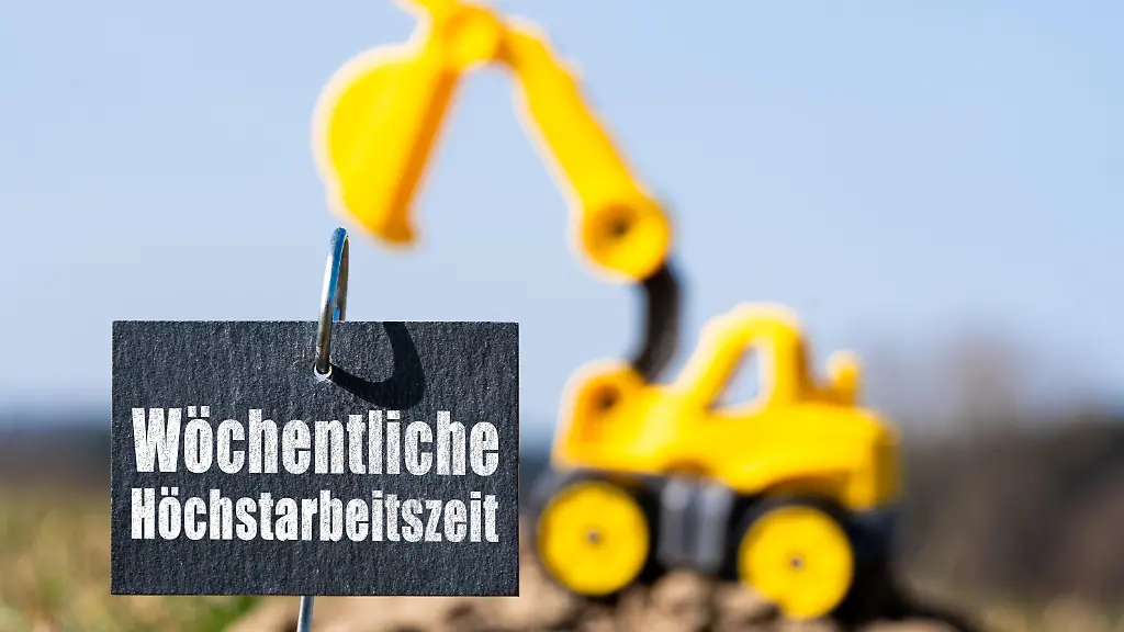 Fotomontage-Ein-Schild-mit-der-Aufschrift-Woechentliche-Hoechstarbeitszeit-steht-vor-einem-kleinen-Bagger-auf-einem-Erdhuegel-Das-Bild-symbolisiert-aktuelle-politische-Debatten-ueber-Arbeitszeitgesetz-Arbeitsmarktregeln-und-Reformen-der-Arbeitszeit