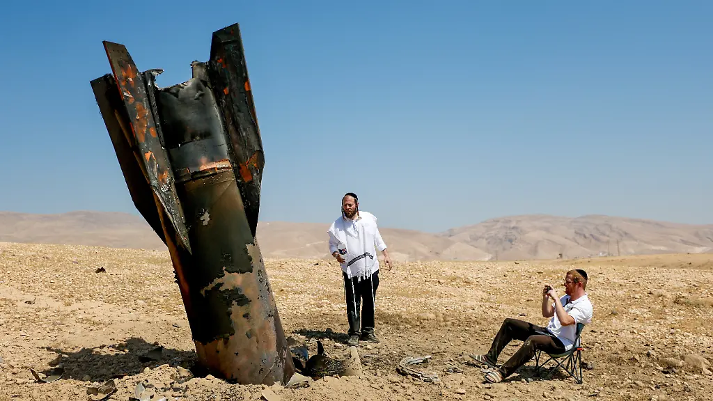 Israelische-ultraorthodoxe-juedische-Maenner-inspizieren-das-Wrack-einer-Rakete-die-nach-einem-iranischen-Angriff-nahe-der-Stadt-Jericho-im-Westjordanland-aus-dem-Boden-ragt
