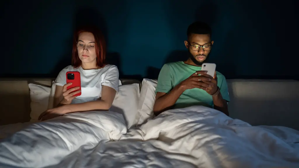 Junges-gemischtrassiges-Paar-liegt-im-Bett-und-benutzt-Smartphones-ohne-zu-sprechen-Junges-gemischtrassiges-Paar-liegt-im-Bett-und-benutzt-Smartphones-ohne-zu-sprechen-model-released-Symbolfoto-Copyright-xZoonar