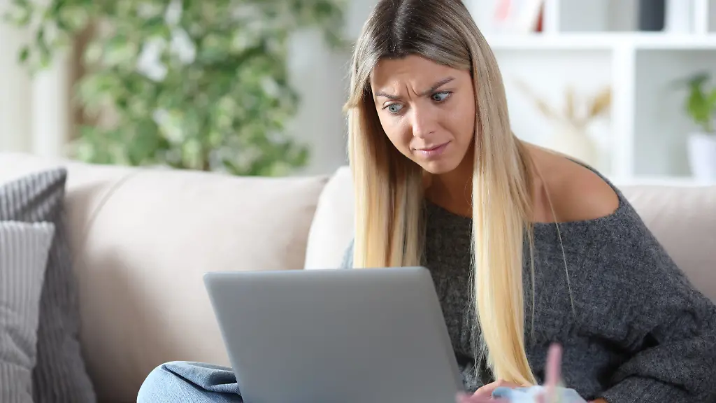 Shocked-woman-checking-strange-content-on-laptop-Shocked-woman-checking-strange-content-on-laptop-sitting-on-a-couch-at-home-model-released-Symbolfoto-Copyright-xAntonioGuillem-1x-Panthermedia101003952