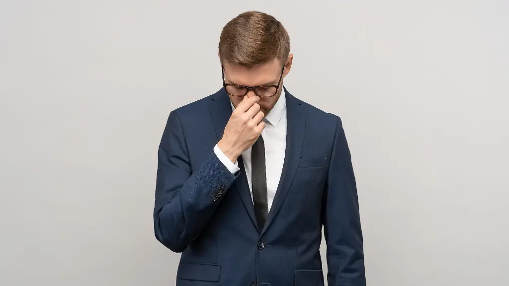 Heartbroken-exhausted-man-businessman-in-suit-office-worker-worried-about-bankruptcy-job-loss-on-grey-background-Upset-guy-feeling-bad-headache-migraine-after-busy-day-burnout-overwork-concept