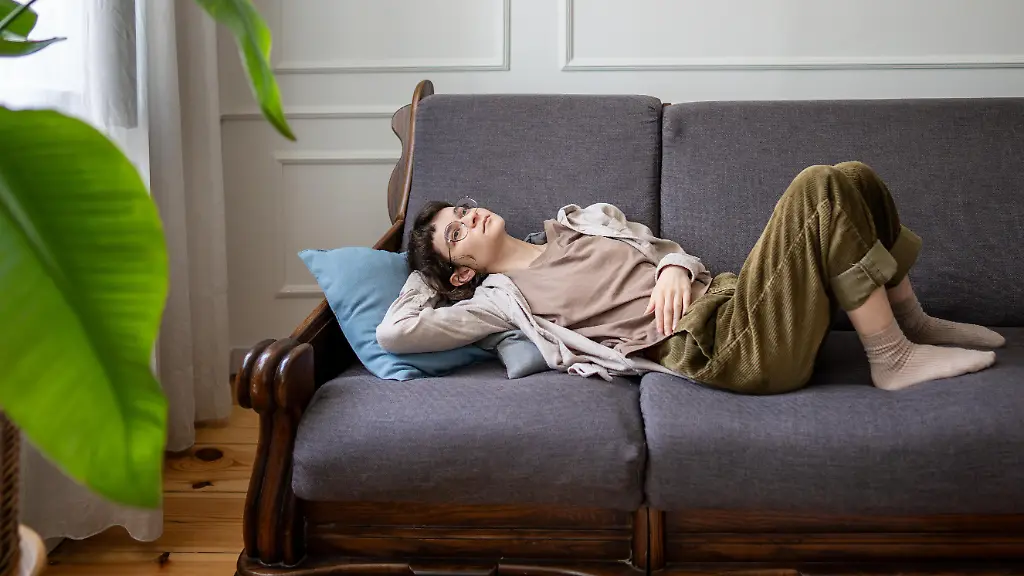 Traumhafte-faule-Frau-auf-Sofa-allein-zu-Hause-verloren-in-Gedanken-mit-indifferenter-Stimmung