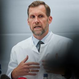Leif Erik Sander sitzt in einem weißen Kittel vor einer weißen Wand.