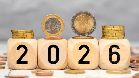 Holzwürfel mit der Jahreszahl 2026 und darauf liegenden Euro-Münzen symbolisieren das Steuerjahr 2026 und Finanzen