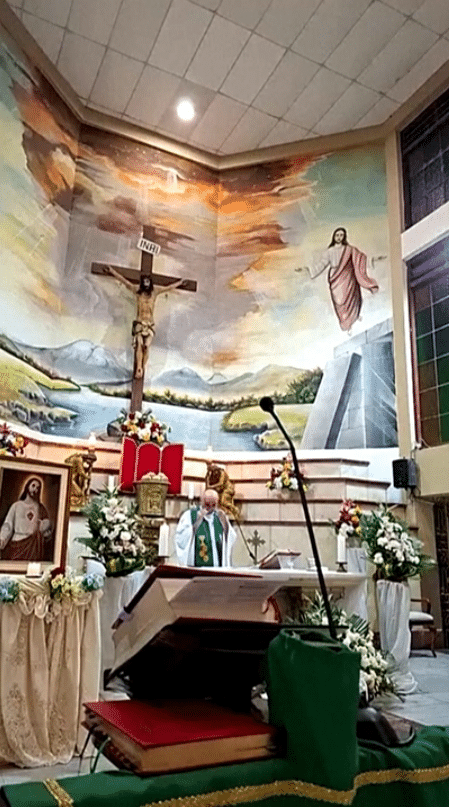 Standbild mit einem Priester am Altar und einem großen Kruzifix an der Wand dahinter.