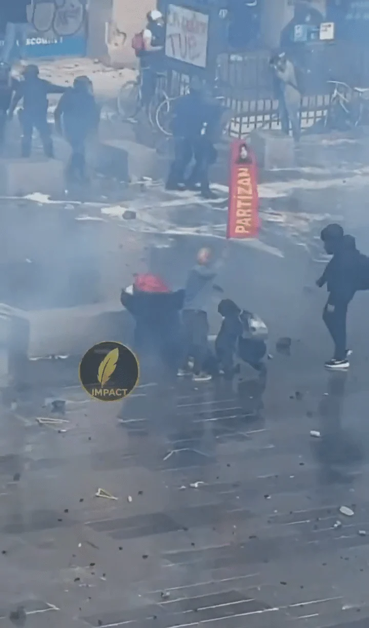 Rote Fahne mit gelbem Schriftzug PARTIZAN bei den Menschen neben der am Boden liegenden Person